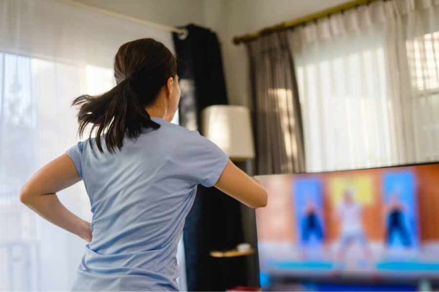 Woman exercising at home with an online workout video on TV.